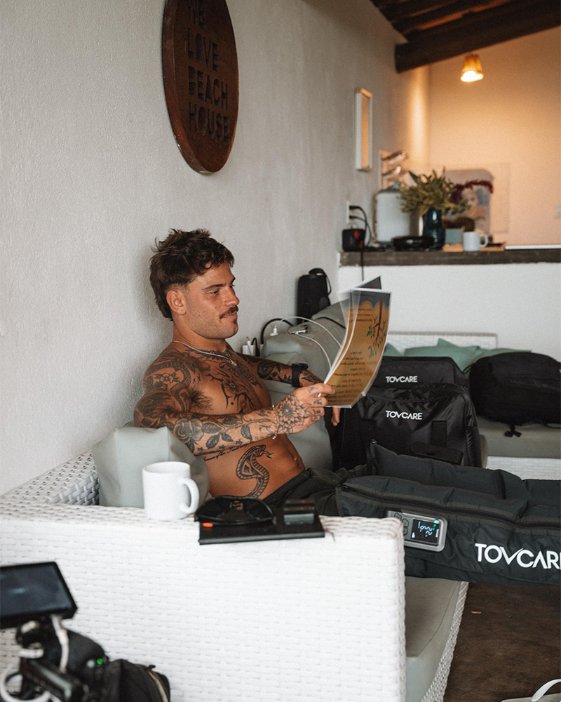 Homem relaxando enquanto usa botas pneumáticas de compressão Tovcare, sentado em um ambiente interno e lendo uma revista.